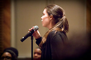 A female student speaks confidently into a microphone before an audience.
